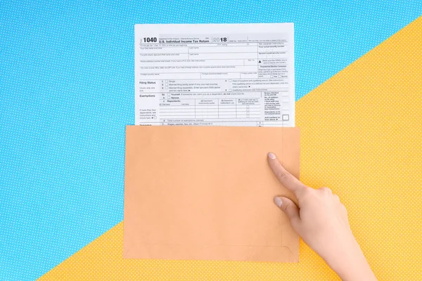 Cropped view of woman pointing with finger at tax form on blue and yellow background — Stock Photo