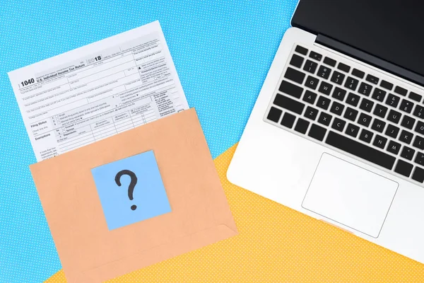 Top view of tax form, blue card with question mark and laptop on blue and yellow background — Stock Photo