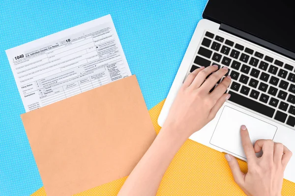 Vista recortada de la mujer escribiendo en el ordenador portátil con formulario de impuestos en el fondo - foto de stock
