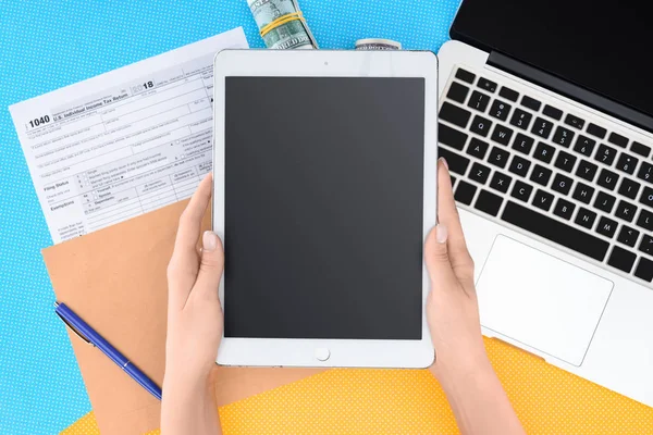 Обрезанный вид женщины, держащей цифровой планшет с чистым экраном на рабочем месте с ноутбуком и налоговой формы на фоне — стоковое фото