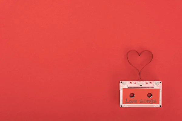 Vista elevada de cassete de áudio com letras canções de amor e símbolo do coração feito de fita isolada em vermelho, conceito dia de São Valentim — Fotografia de Stock