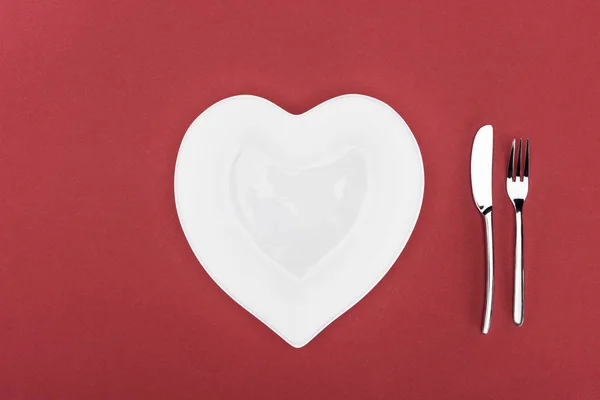 Vista elevada de la placa en forma de corazón y cubiertos aislados en rojo, San Valentín concepto de día - foto de stock