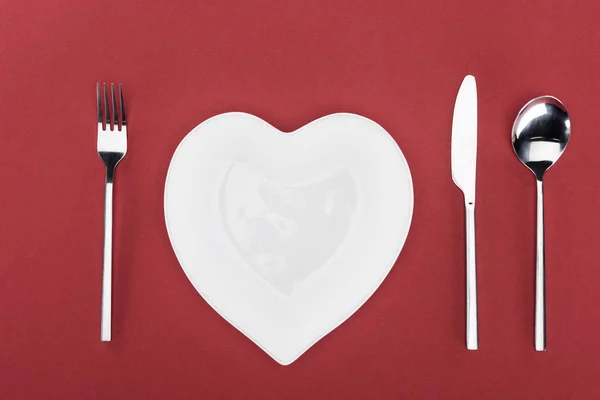 Vue d'en haut de la plaque en forme de coeur et couverts isolés sur rouge, concept St Valentin — Photo de stock