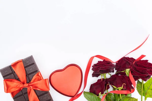 Вид зверху шоколаду, загорнутий святковою стрічкою, червоні троянди та серцеподібна подарункова коробка ізольовані на білому, концепція дня Святого Валентина — стокове фото