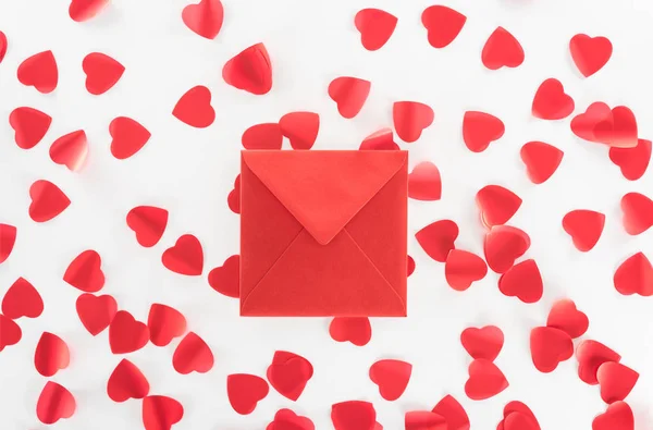 Acostado plano con sobre rojo y símbolos rojos del corazón aislados en blanco, San Valentín concepto de día - foto de stock