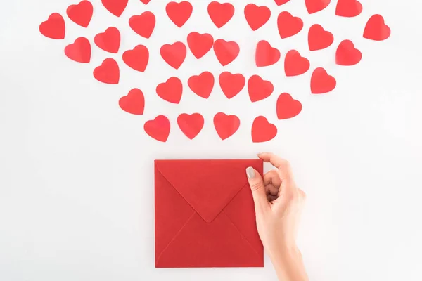 Частковий вигляд жінки, що тримає конверт під десятками червоних символів серця ізольовані на білому, концепція святого Валентина — стокове фото