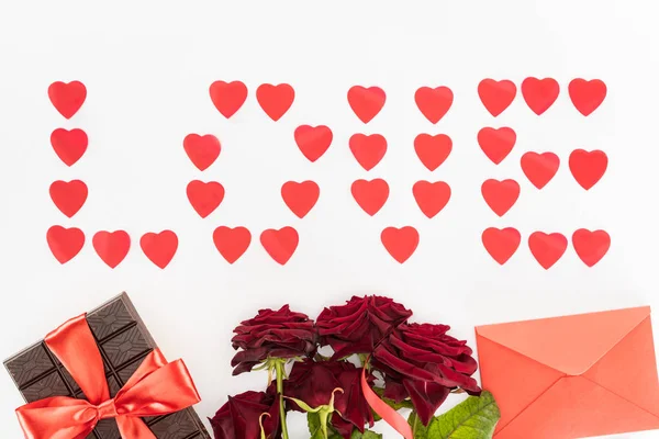 Vue du haut de lettrage amour fait de symboles de coeur, chocolat enveloppé par ruban festif, roses rouges et enveloppe isolée sur blanc, concept St Valentin — Photo de stock