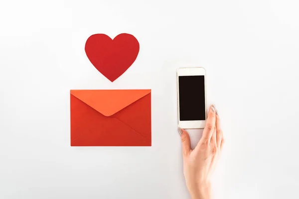 Imagen recortada de la mujer sosteniendo teléfono inteligente con pantalla en blanco cerca del símbolo del corazón y sobre rojo aislado en blanco, San Valentín concepto de día - foto de stock