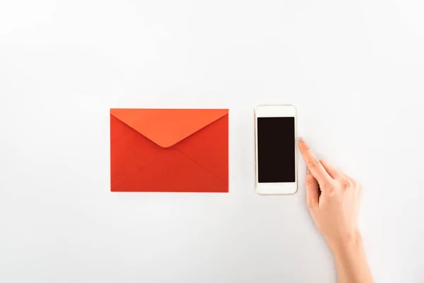 Vista parcial de la mujer sosteniendo teléfono inteligente con pantalla en blanco cerca de sobre rojo aislado en blanco, San Valentín concepto de día - foto de stock