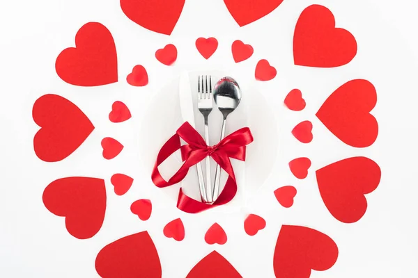Erhöhte Ansicht des Bestecks umhüllt von roter festlicher Schleife, umgeben von Herzsymbolen, isoliert auf weißem, Valentinstag-Konzept — Stockfoto