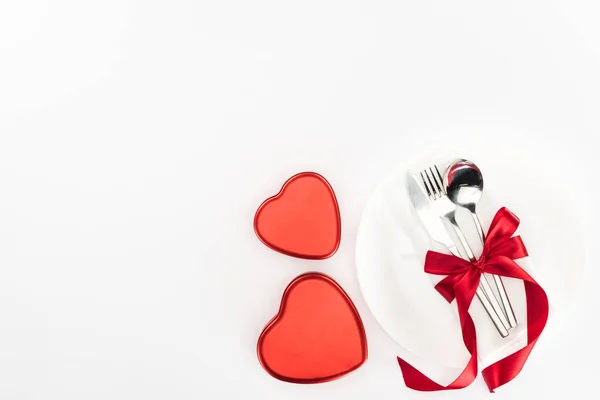 Vista desde arriba de la placa con cubiertos envueltos por cinta festiva cerca de cajas de regalo en forma de corazón aisladas en blanco, concepto de día de San Valentín st - foto de stock