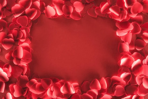 Vue du haut des pétales décoratifs en forme de coeur sur fond rouge, concept de Saint-Valentin — Photo de stock