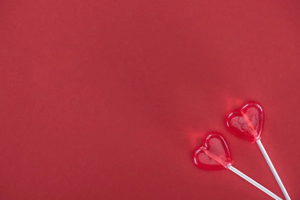 Vista superior de dos piruletas en forma de corazón sobre fondo rojo, concepto de día de San Valentín - foto de stock
