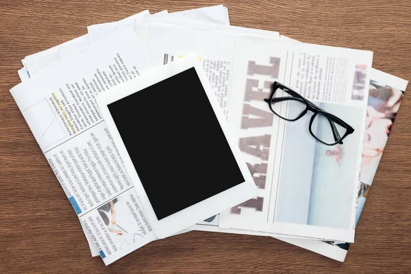 Vista superior do tablet com tela em branco, óculos e jornais em mesa de madeira — Fotografia de Stock