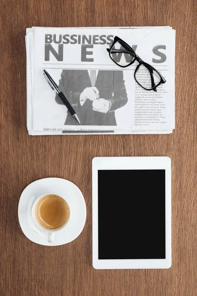 Vista sopraelevata di tazza di caffè, tablet con schermo bianco e giornale commerciale su tavolo in legno — Foto stock