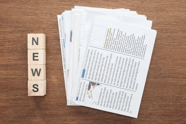 Top view of wooden cubes with word news and newspapers on wooden tabletop — Stock Photo