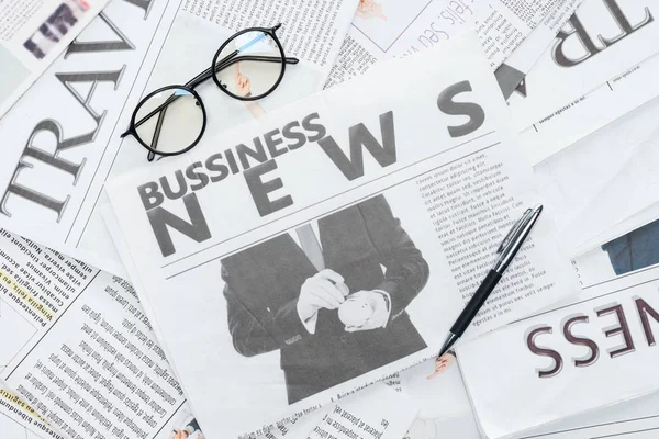 Top view of eyeglasses and pen on business newspapers — Stock Photo