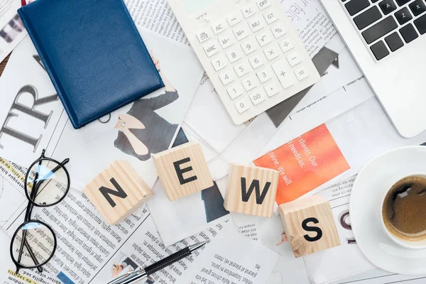 Draufsicht auf Holzwürfel mit Word News, Laptop und Taschenrechner auf Zeitungen — Stockfoto