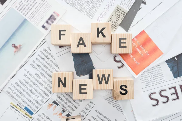 Top view of wooden cubes with words fake news on newspapers — Stock Photo