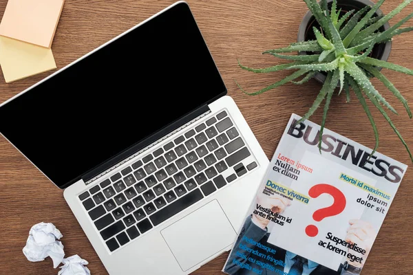 Top view of laptop, business magazine and potted plant on wooden tabletop — Stock Photo