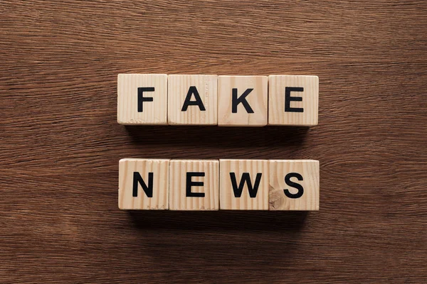 Top view of wooden cubes with words fake news on newspapers on wooden tabletop — Stock Photo