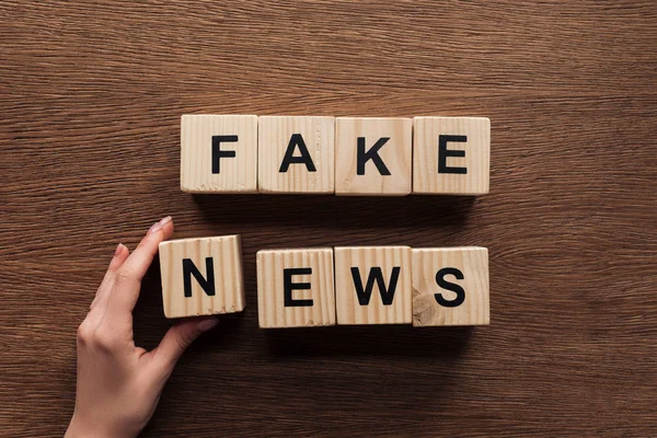 Cropped image of journalist taking wooden cubes with words fake news at wooden table — Stock Photo