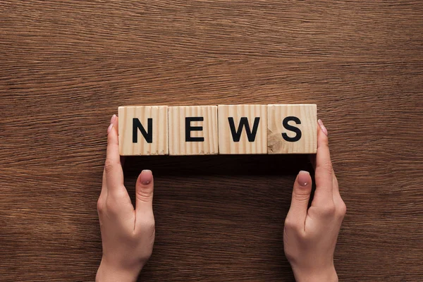 Image recadrée d'un journaliste tenant des cubes en bois avec des nouvelles de mots à table en bois — Photo de stock