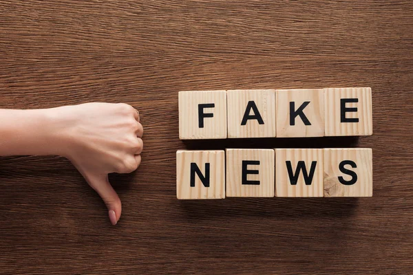 Ausgeschnittenes Bild eines Journalisten, der den Daumen auf Holzwürfel mit Worten Fake News am Holztisch zeigt — Stockfoto