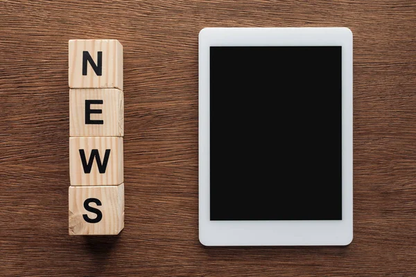 Верхний вид планшета с чистым экраном и деревянными кубиками со словом новости на деревянном столе — стоковое фото