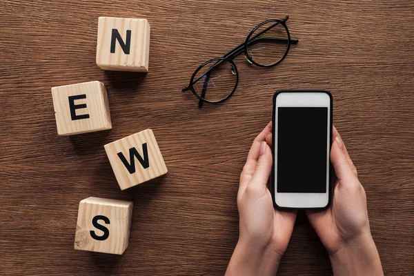 Immagine ritagliata di giornalista in possesso di smartphone, cubi di legno con notizie parola su tavolo di legno — Foto stock
