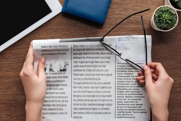 Imagen recortada de periodista sosteniendo periódico y vasos en mesa de madera — Stock Photo