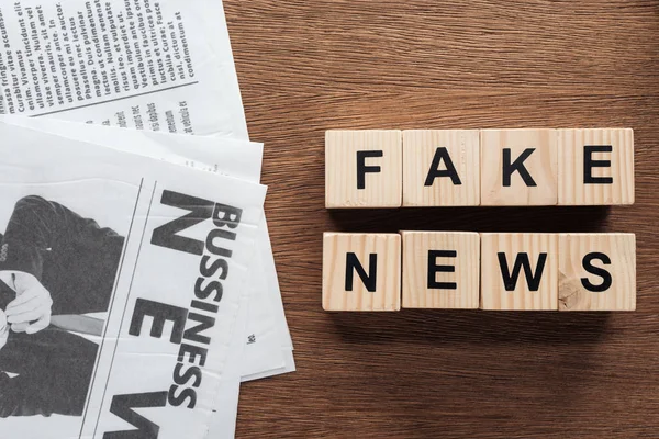 Ansicht von Holzwürfeln mit Wörtern Fake News und Zeitungen auf hölzerner Tischplatte — Stockfoto
