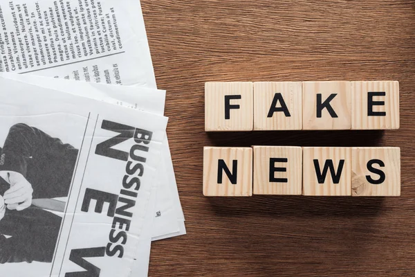 Top view of wooden cubes with words fake news and newspapers on wooden tabletop — Stock Photo