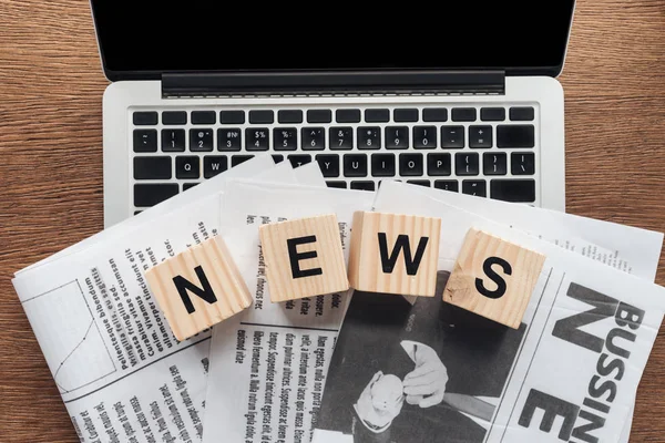 Top view of wooden cubes with word news and newspapers on laptop on wooden tabletop — Stock Photo