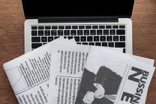 Top view of newspapers and laptop on wooden tabletop — Stock Photo