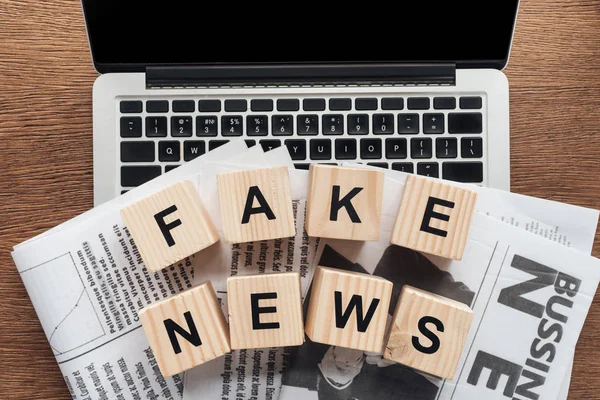 Top view of wooden cubes with words fake news and newspapers on laptop on wooden tabletop — Stock Photo