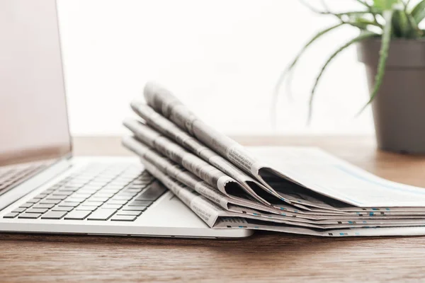 Laptop, plant and stack of newspapers on wooden tabletop — Stock Photo