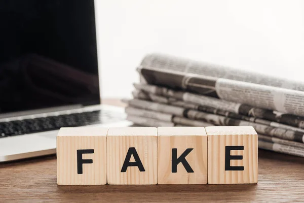 Wooden cubes with word fake, laptop and newspapers on wooden tabletop — Stock Photo