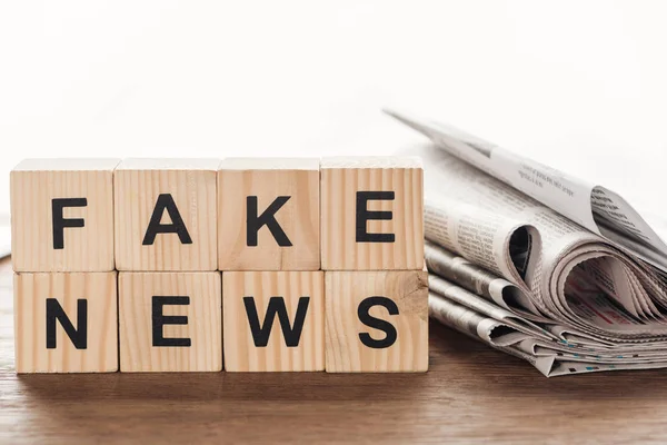 Holzwürfel mit Wörtern Fake News und Zeitungen auf Holztischplatte — Stockfoto