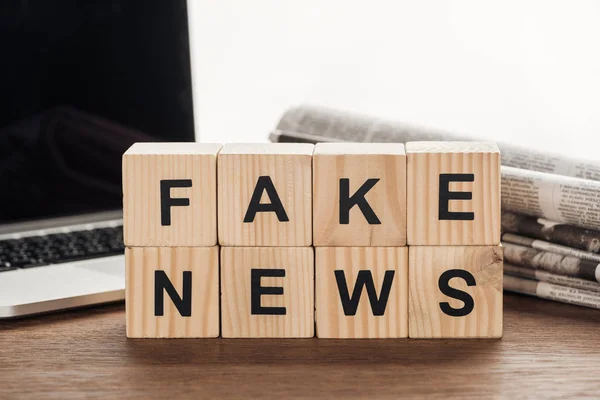 Cubi di legno con parole fake news, laptop e giornali su tavolo di legno — Foto stock