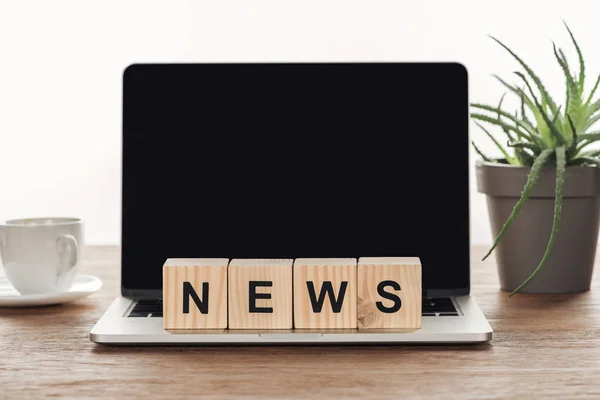 Cubos de madera con noticias de la palabra en el ordenador portátil con pantalla en blanco en la mesa de madera - foto de stock