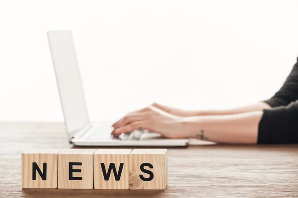 Cropped image of journalist working at laptop, wooden cubes with word news on tabletop — Stock Photo