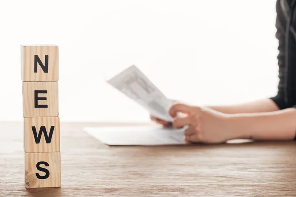 Cropped image of journalist reading newspaper, wooden cubes with word news on wooden table — Stock Photo