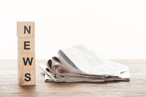 Cubes en bois avec nouvelles mot et journaux sur table en bois — Photo de stock