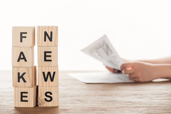 Cropped image of journalist reading newspaper, wooden cubes with words fake news at wooden table — Stock Photo