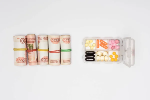 Top view of money rolls and pills in plastic container isolated on grey — Stock Photo