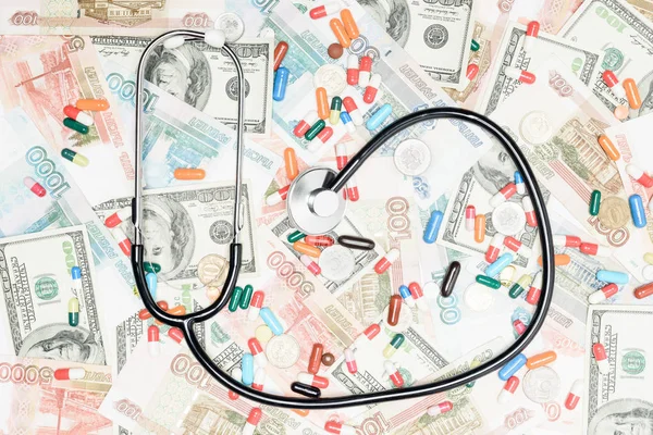 Top view of multicolored pills, coins and stethoscope on money background — Stock Photo