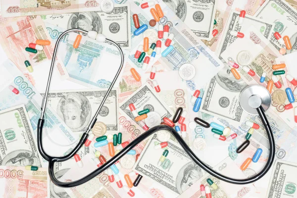 Top view of multicolored pills, coins and stethoscope on cash background — Stock Photo
