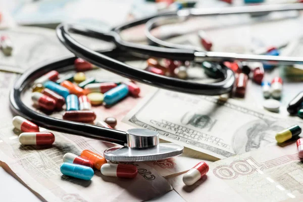 Close up of multicolored pills and stethoscope on money background — Stock Photo