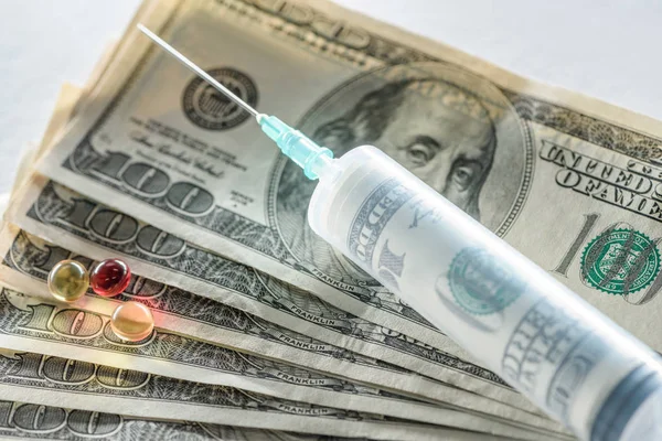 Gros plan de la seringue avec injection d'argent et pilules sur les billets en dollars — Photo de stock